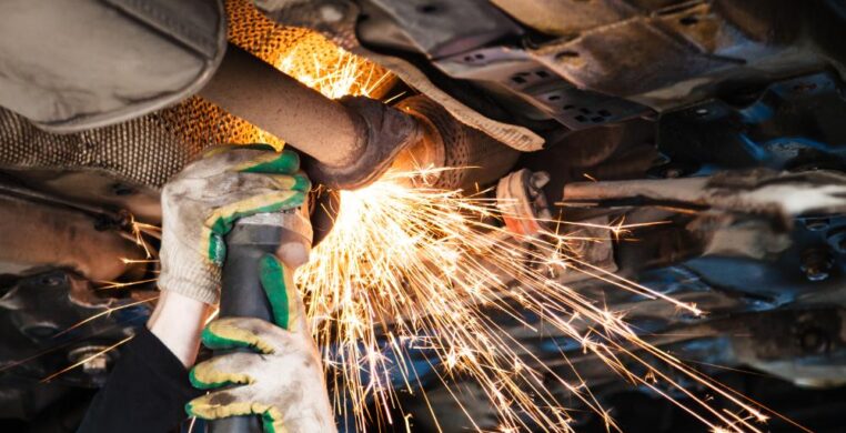 Mechanic performing exhaust repair in Nottingham while car is elevated on hydraulic lift.