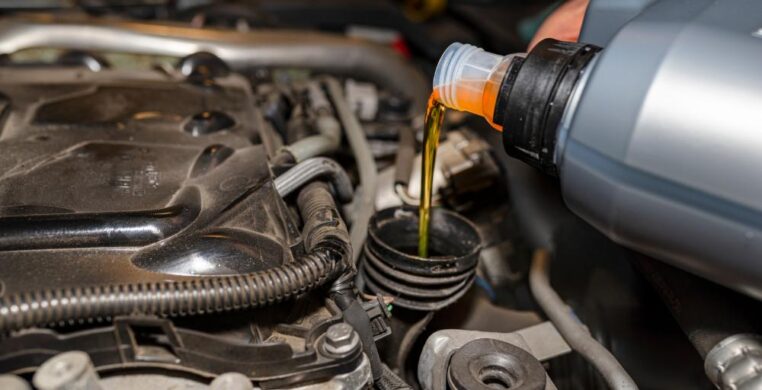 Mechanic performing car service in Nottingham, pouring engine oil into a car’s engine bay with tools and workshop in background.
